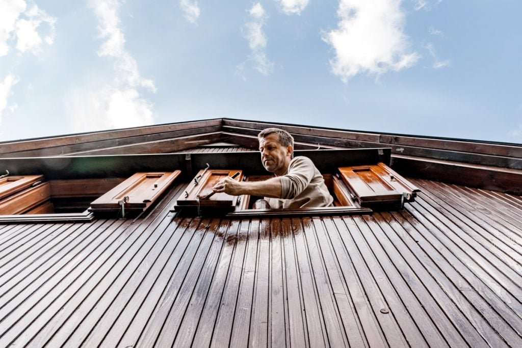 A man puts a fresh coat of paint on his shutters. 