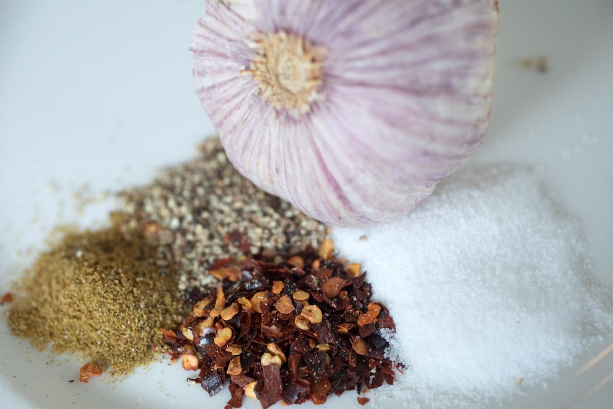 Herbs and spices sit in a bowl next to garlic. 